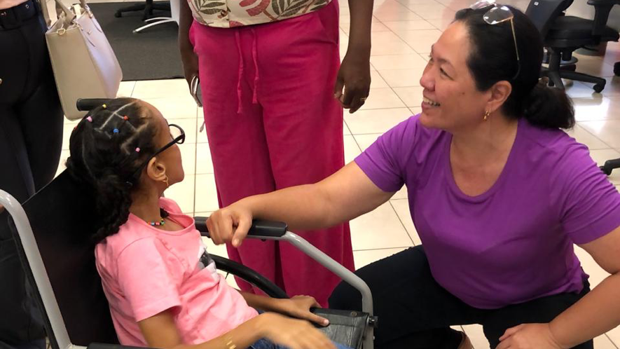 Recepção de uma criança sentada em uma cadeira de rodas e uma colaboradora sorrindo