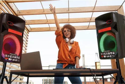 DJ mulher negra no centro da tela, com cabelos cacheados controlando uma mesa de som, no meio de 2 caixas de som da Polyvox em pedestais