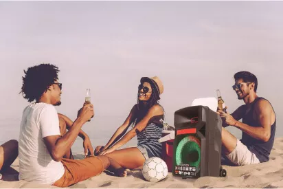 Grupo de 3 amigos na praia curtindo, rindo e conversando, escutando música na caixa de som da Polyvox XC-810