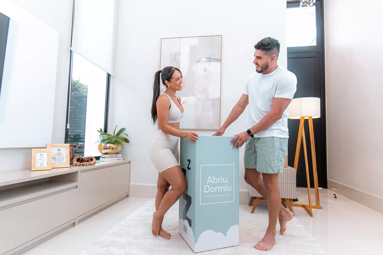 Casal organizando o quarto e posicionando o colchão antes da rotina de descanso