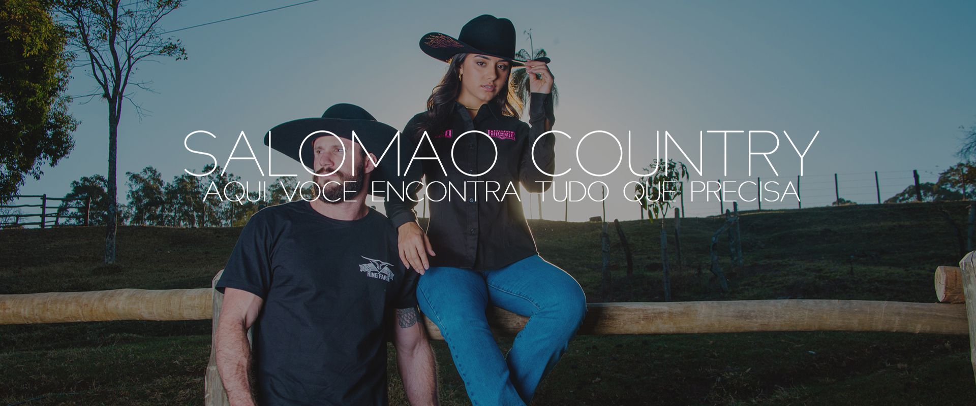 Uma imagem onde tem um casal encostado em uma cerca, atrás um por do sol.