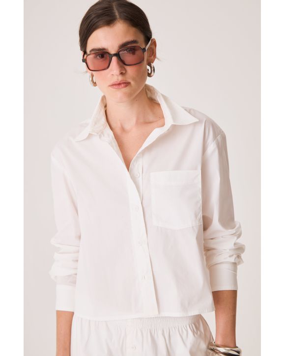 Camisa feminina cropped branca com leve transparência, mangas longas com botão, bolso lateral e gola tradicional