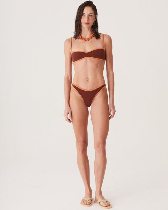 A modelo veste um Top Luna Café com decote em V profundo, alças ajustáveis e lycra premium. Peça da collab August Swim + NK Store com design sofisticado.