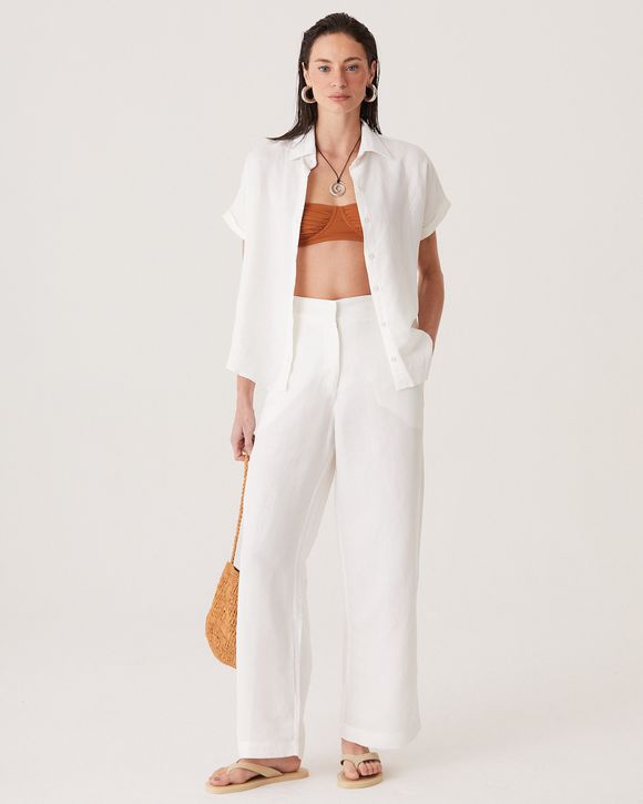 Modelo esta vestindo uma calça pantacourt feminina em linho off white com corte amplo e acabamento sofisticado.