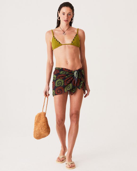 A Modelo esta com uma Pareô Gabi com estampa de conchas em algodão, versátil e elegante para o dia na praia, amarrada na cintura.