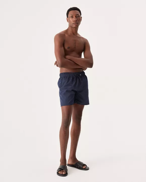 O Modelo esta vestindo um Short masculino azul noite com cós elástico e boxer interno, ideal para conforto e estilo em ambientes à beira da água.