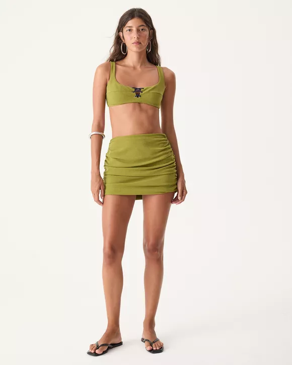 A modelo veste uma Mini saia de biquíni verde matcha com drapeado lateral, hot pants interna e modelagem justa ao corpo.