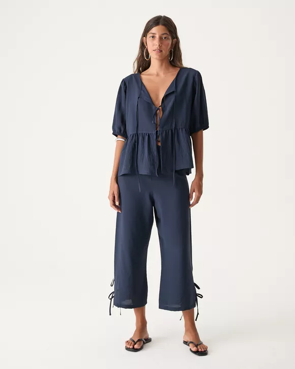 A Modelo esta vestindo uma Calça pantacourt azul noite feminina com amarrações laterais e modelagem fluida.