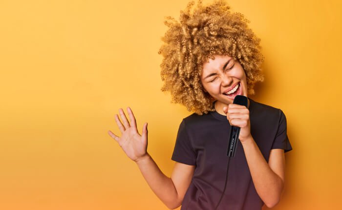 Mulher negra de cabelos cacheados cantando, em um fundo laranja, com o microfone XM-108 da Polyvox?rel=0